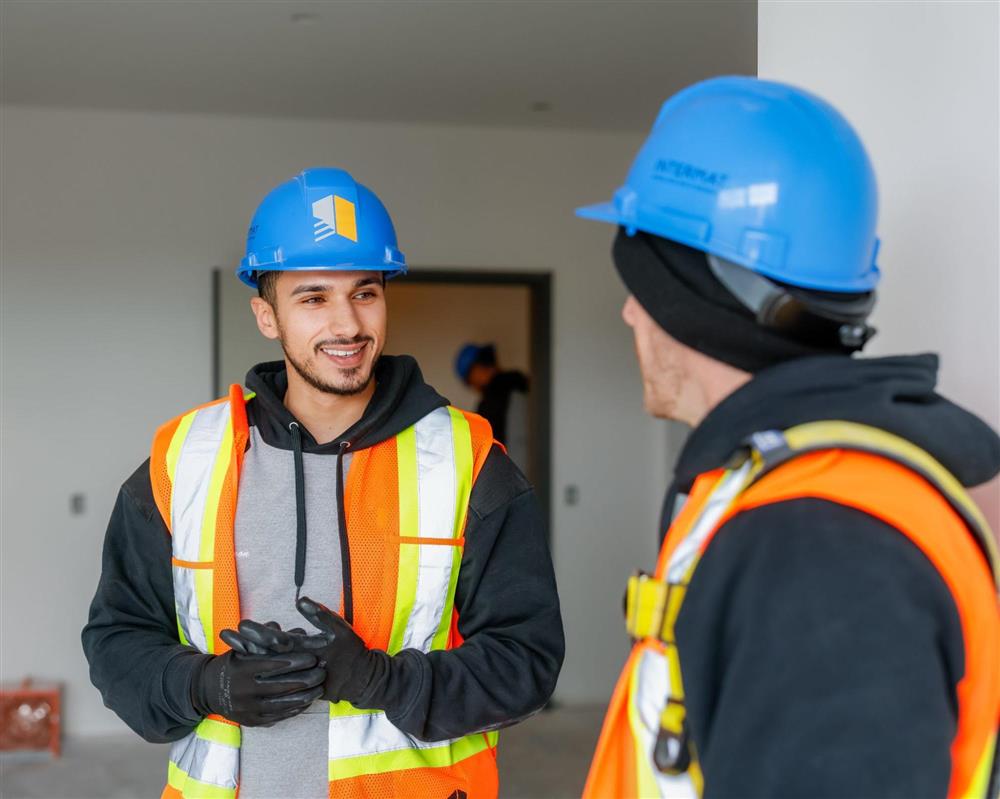 Deux travailleurs de la construction portant des casques de sécurité et des vestes haute visibilité discutent à l'intérieur d'un chantier en phase de finition, illustrant la coordination et l'accompagnement sur un projet de construction à Ottawa.